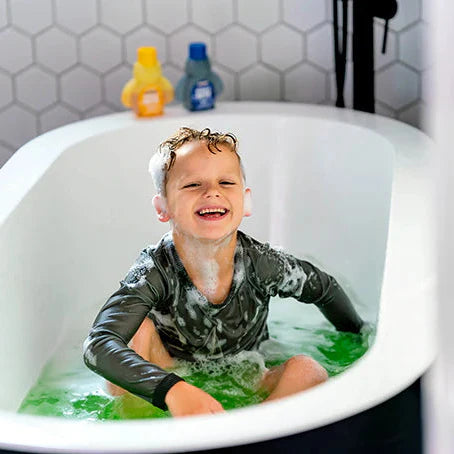 Child in a bathtub with green water and bath products on the edge.
