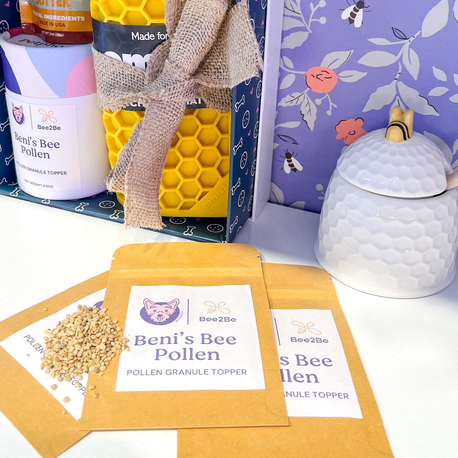 Bee-themed products including a yellow honeycomb-shaped container, a white jar, and packets of pollen on a floral background.