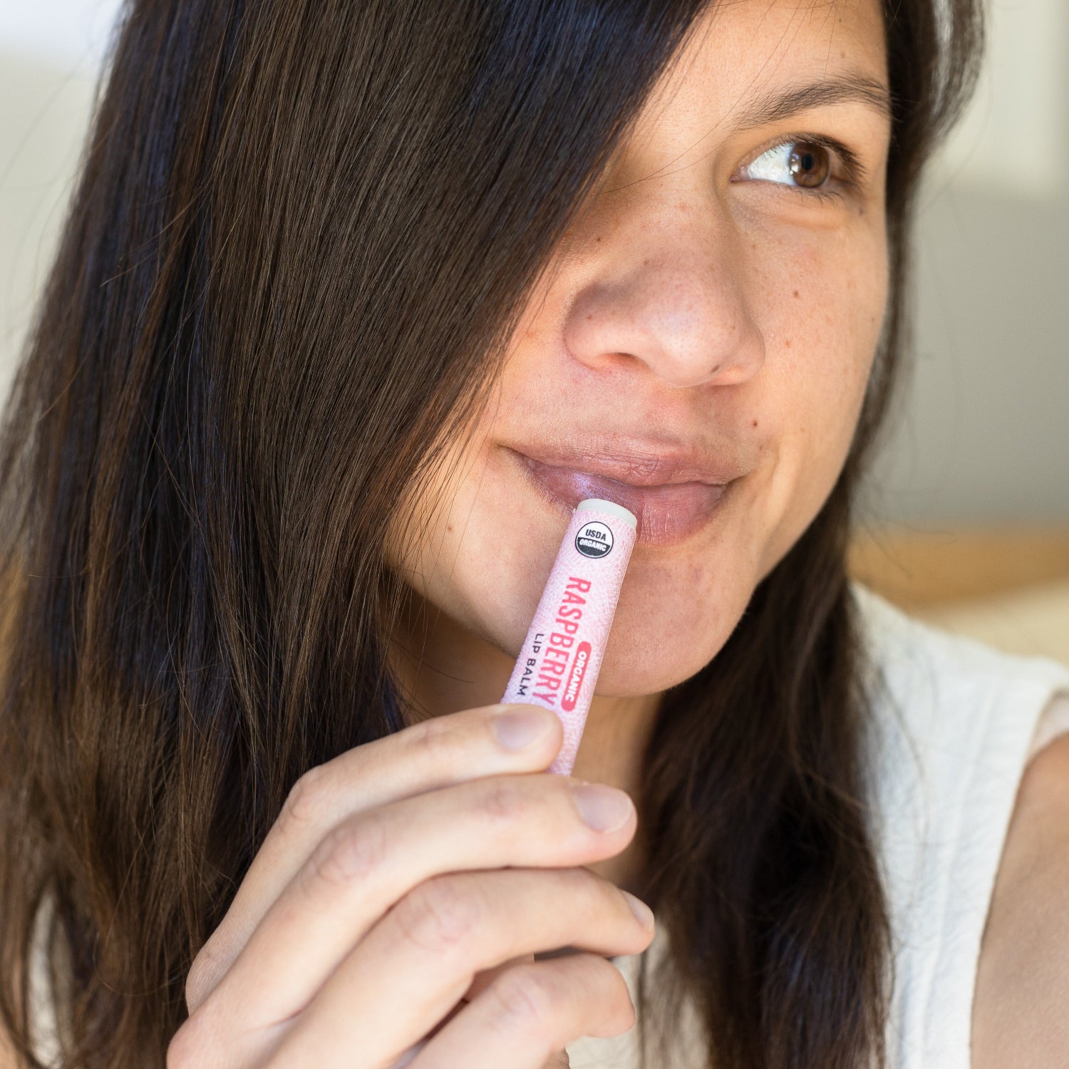 Woman holding a pink lip balm with visible branding
