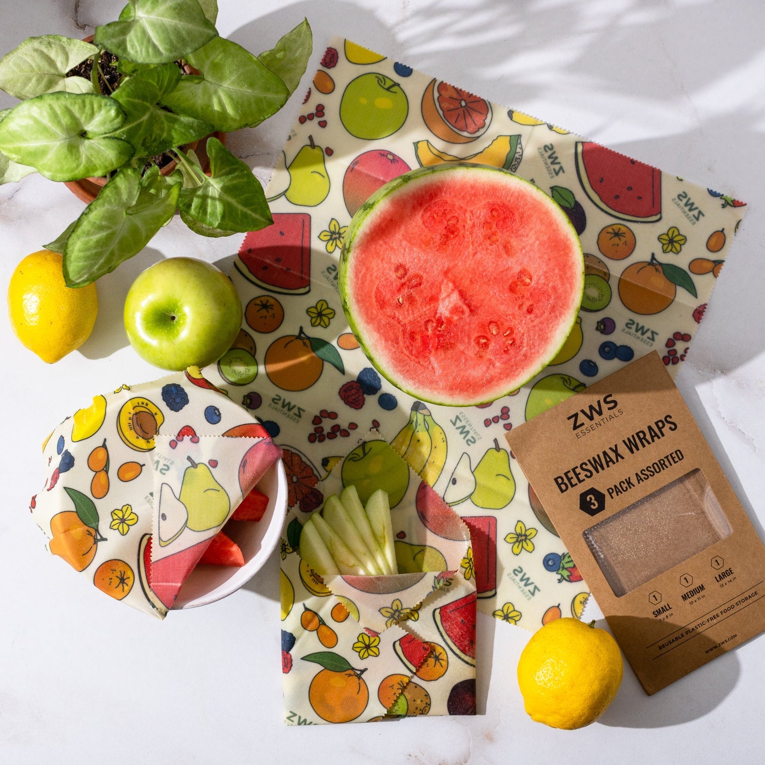 Colorful beeswax wraps with a half-cut watermelon and lemons on a white surface.