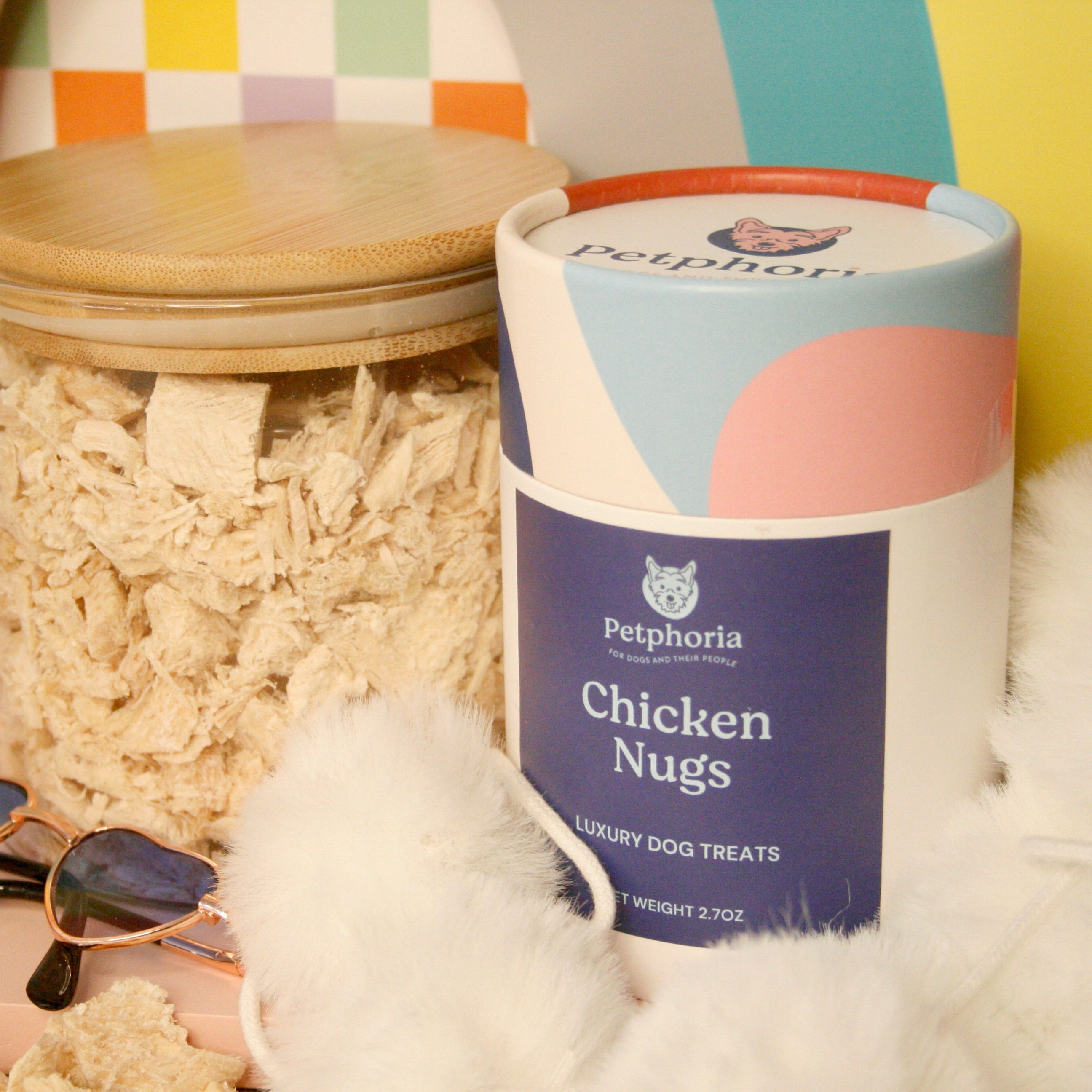 Petfood container labeled 'Chicken Nugs' with a jar of dog treats and sunglasses on a colorful background