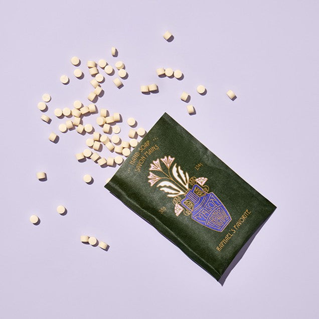 Green packet with floral design and text on a light purple background with scattered pills.